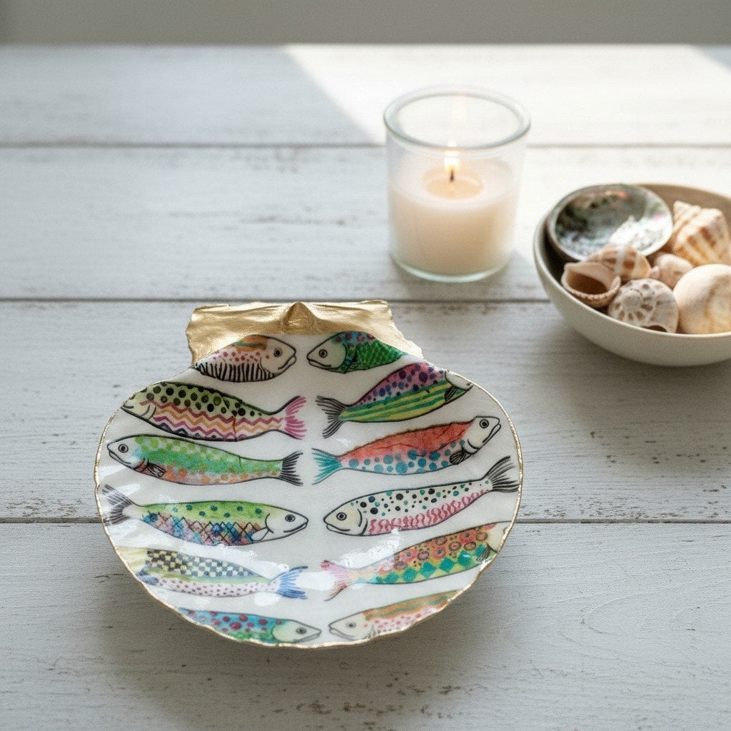 Colorful fish scallop shell trinket dish styled beside a candle and bowl of shells